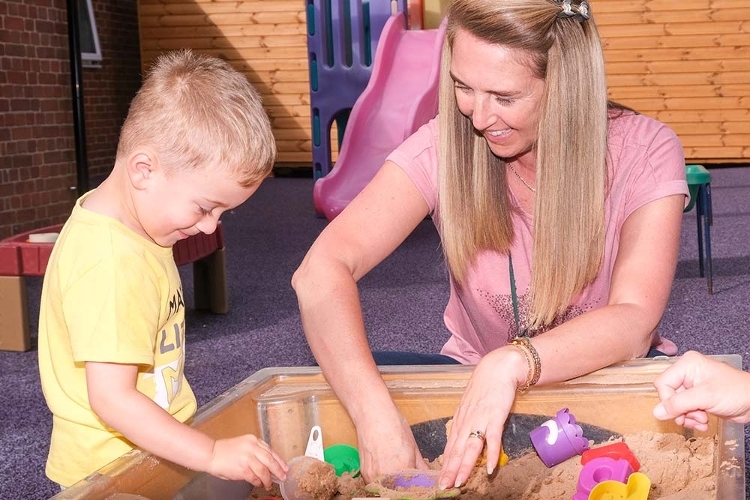 An image of a woman and a child playing in a sand pit.