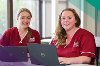A photo of two reablement carers smiling whilst working on their laptops.